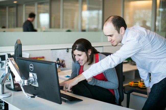 Two Brooks Bell employees talk at a computer